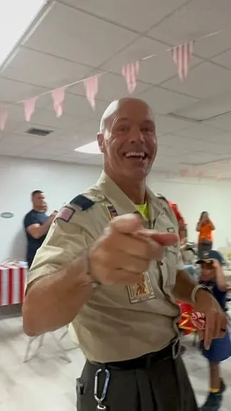 Mr. Bob, Cubmaster, grins and points at the camera during circus night, with Cub Scouts dancing around him.