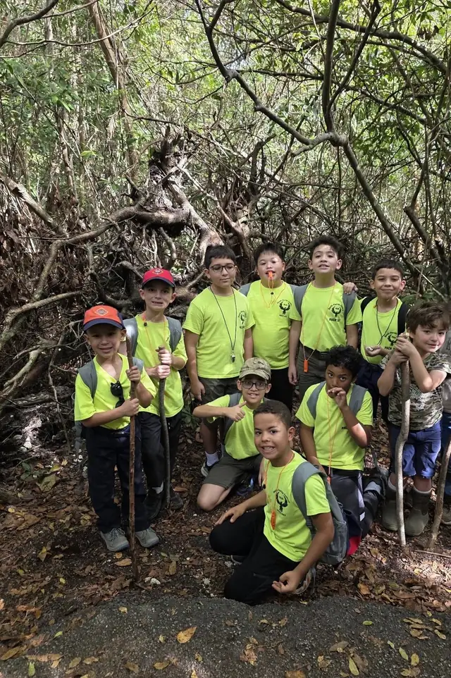 Cub Scouts in matching neon-yellow shirts on a wooded trail hike.