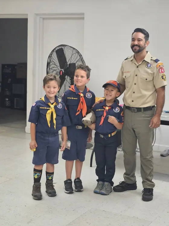 Mr. Danny, Wolves Den Leader, stands with younger Cub Scouts at an indoor pack meeting.